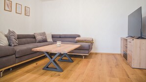 Ett modernt vardagsrum med en hörnsoffa, ett soffbord i trä, en tv placerad på ett träskåp och inramade konstverk på väggen.