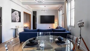 A modern living room with a glass dining table, blue sofa, and a mounted TV. - Boutique African-inspired Luxury 1BR in Central Cape Town with Parking (Cape Town)