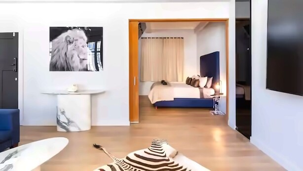 A modern hotel room with a large bed, a desk, a chair, a zebra-patterned rug, and a mounted TV. - Boutique African-inspired Luxury 1BR in Central Cape Town with Parking (Cape Town)
