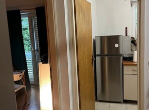 Eine Küche mit einem Edelstahl-Kühlschrank, einer Holztür und Blick ins Freie.