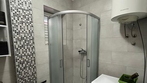 A corner shower with a glass door, a white washing machine, and a green basket on the countertop. - Dubrovnik Gruž Studio (Dubrovnik)