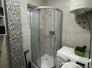 Ein modernes Badezimmer mit einer gläsernen Duschkabine, einer weißen Waschmaschine und einer gefliesten Wand mit Mosaikmuster.