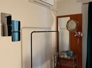 Ein Zimmer mit einem Wäscheständer aus Metall, einem Spiegel und einer Wandklimaanlage.
