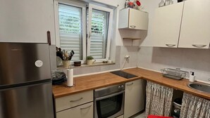 A kitchen with a refrigerator, oven, sink, and window with blinds. - Dubrovnik Gruž Studio (Dubrovnik)