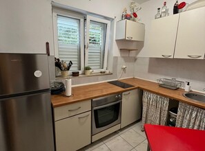 Ett kök med kylskåp, ugn, diskho och ett fönster med persienner.
