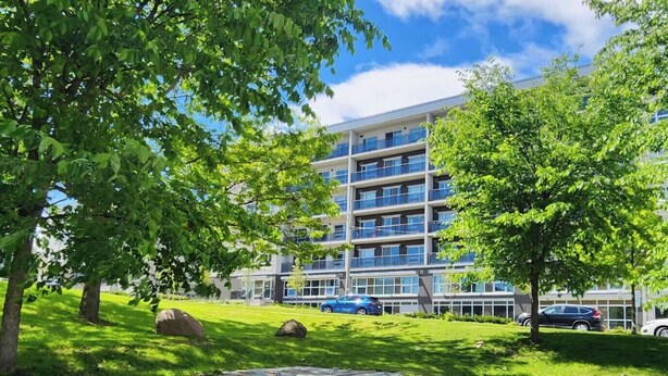 A multi-story building with balconies, surrounded by lush green trees and grass.
