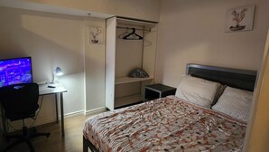 A bedroom with a bed, a desk with a computer, a chair, a wardrobe, and a nightstand.