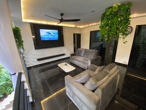 Ein modernes Wohnzimmer mit Flachbildfernseher, grauen Sofas, einem Couchtisch und einem Deckenventilator.
