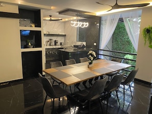 Un espace repas moderne avec une table en bois et des chaises noires, une cuisine avec un dosseret en marbre et un balcon offrant une vue sur la verdure.