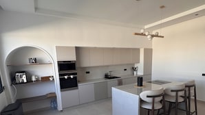 Eine moderne Küche mit weißen Schränken, einer zentralen Kochinsel, Barhocker und einer Deckenleuchte.