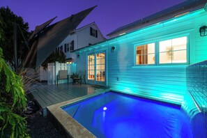 A swimming pool with a wooden deck, a house with teal exterior lighting, and a white fence. - Marvelous Newly Renovated 2-bedroom Dog Friendly home close to Duval & Beach (Key West)