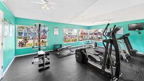 Une salle de sport équipée de matériel d’exercice, dotée d’un ventilateur au plafond et de grandes fenêtres offrant une vue sur l’extérieur.