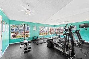 A gym with exercise equipment, a ceiling fan, and large windows with a view of the outdoors.
