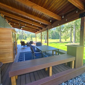 Un espacio exterior cubierto con una terraza de madera, una mesa, sillas y vistas a un paisaje cubierto de césped.