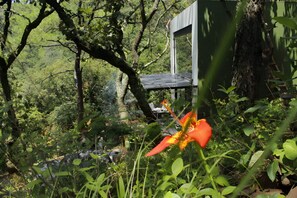 A rustic wooden structure in a forested area with a chair and a table nearby.