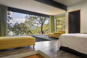 A modern bedroom with a large window, a bed, a yellow armchair, and a sofa.