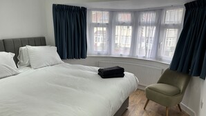 Un dormitorio con cama, una silla, un radiador y un ventanal con cortinas.