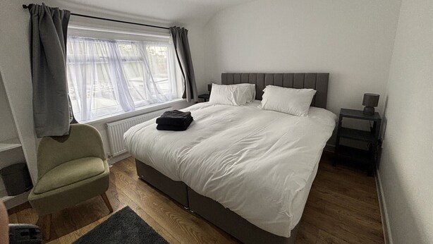 Un dormitorio con una cama, una silla, una mesita de noche y una ventana con cortinas.