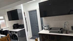 Una cocina compacta con lavadora, cafetera y lavabo.