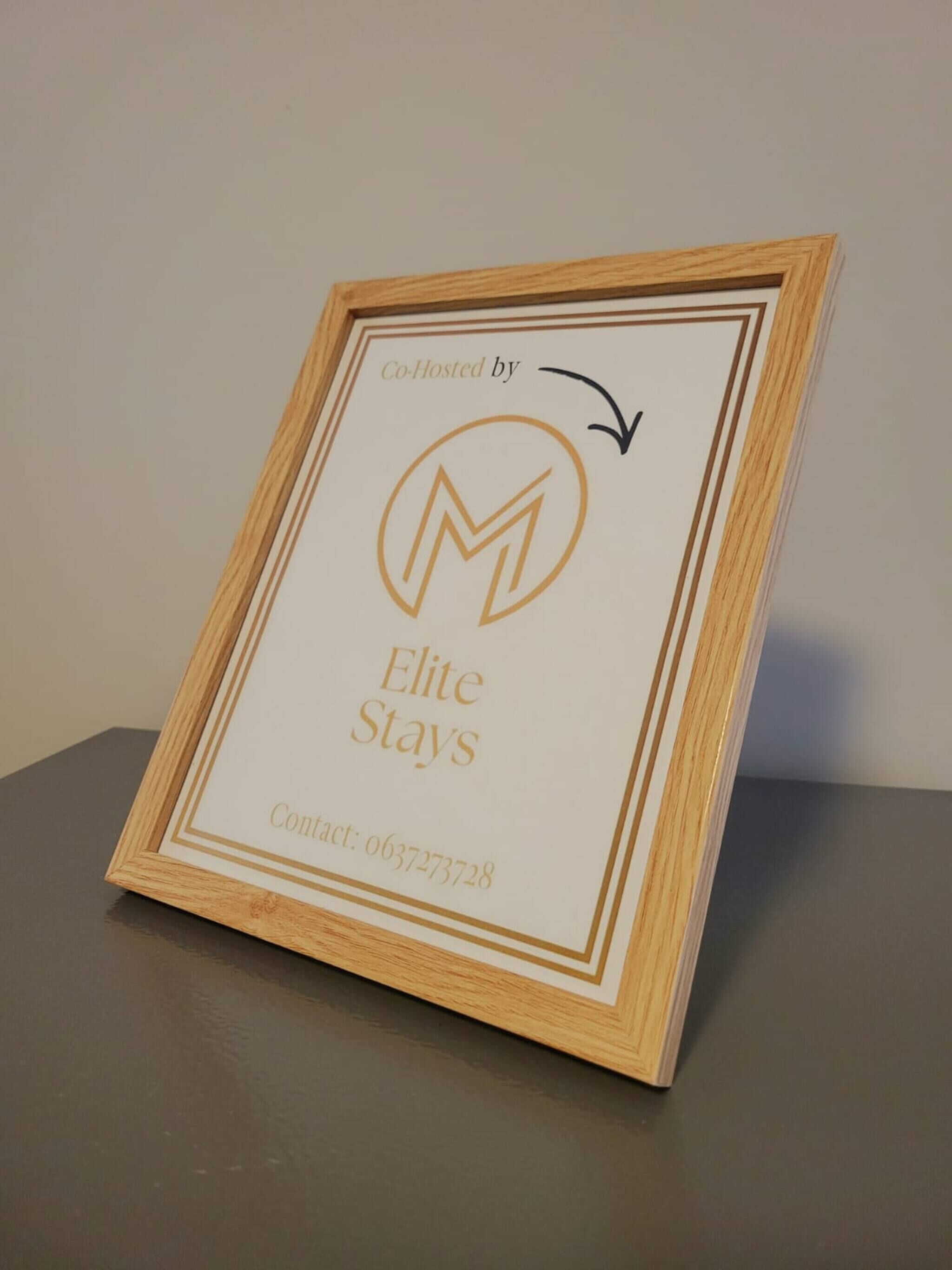 Ein gerahmtes Schild mit dem Text 'Co-Hosted by Elite Stays' und einer Kontaktnummer.