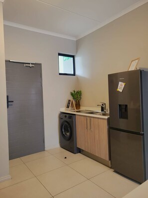 Una cocina compacta con lavadora, refrigerador y un ventanal pequeño.