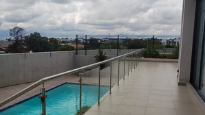 A rooftop pool with a metal railing, a clear view of the sky, and a distant cityscape. - Cozy 1-bed in Midrand (Johannesburg)