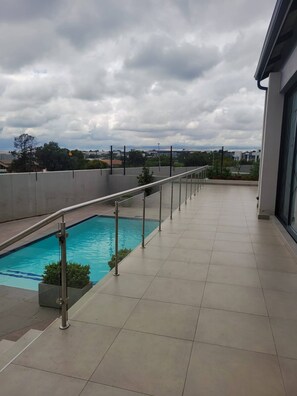 Una piscina en la azotea con barandilla metálica, vista despejada del cielo y un horizonte urbano lejano.