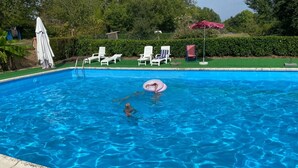 Ein Schwimmbecken mit Kind und Erwachsenem, umgeben von Liegestühlen und Sonnenschirmen.