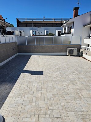 A rooftop terrace with a tiled floor, a metal fence, and an air conditioning unit.