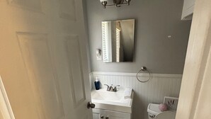 Kylpyhuone, jossa on valkoinen pesuallas, peili ja wc-istuin.