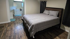 Quarto com cama, ventilador de teto, janela e banheiro visível ao fundo.