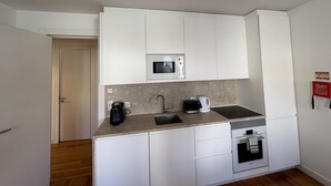 A compact kitchen with white cabinets, a built-in microwave, a coffee maker, and a small oven. - Alfama Premium (Lisbon)