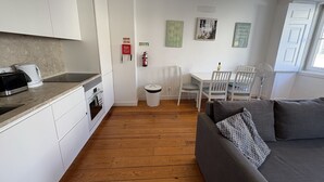 A modern kitchen with white cabinets, a dining area with white chairs, and a grey sofa. - Alfama Premium (Lisbon)