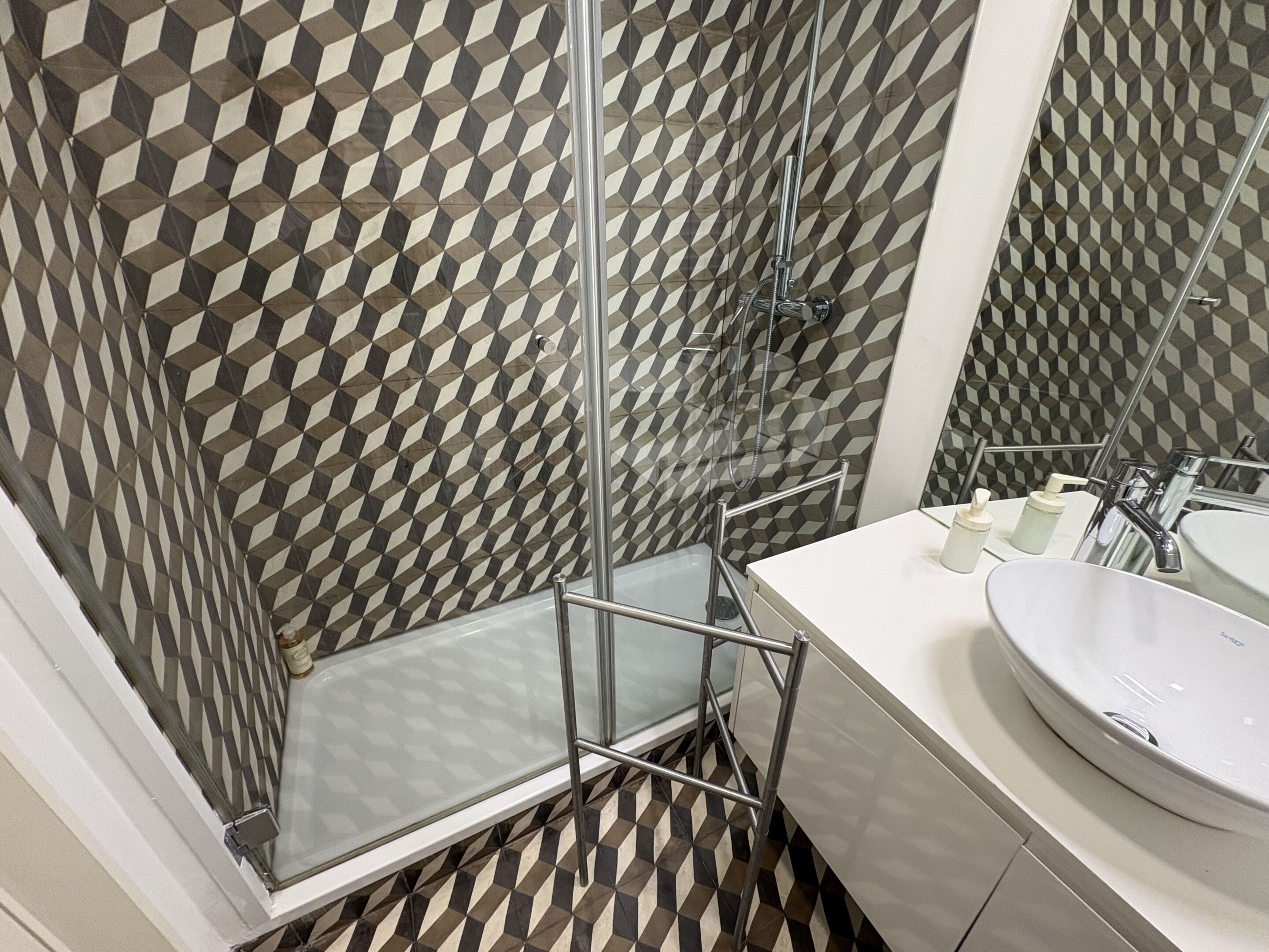 Ein modernes Badezimmer mit Wandpaneelen mit geometrischem Muster, einer Glasdusche, einem weißen Waschbecken und einem Spiegel.