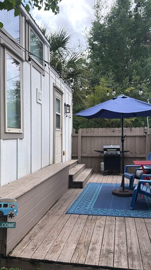 A deck with a barbecue grill, outdoor furniture, and a welcome sign. - Private Tiny Home w/ Courtyard, Grill & Quiet Location – Sleeps 2 (Pensacola)