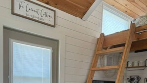 A wooden ladder leaning against a kitchen counter with shelves above, a door with a window, and a sign above the door. - Private Tiny Home w/ Courtyard, Grill & Quiet Location – Sleeps 2 (Pensacola)