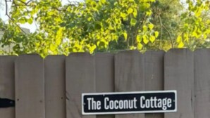 A wooden fence with a sign that reads 'The Coconut Cottage.' - Private Tiny Home w/ Courtyard, Grill & Quiet Location – Sleeps 2 (Pensacola)