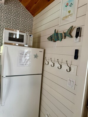 A kitchen with a white refrigerator, a microwave, and a wall-mounted clock. - Private Tiny Home w/ Courtyard, Grill & Quiet Location – Sleeps 2 (Pensacola)