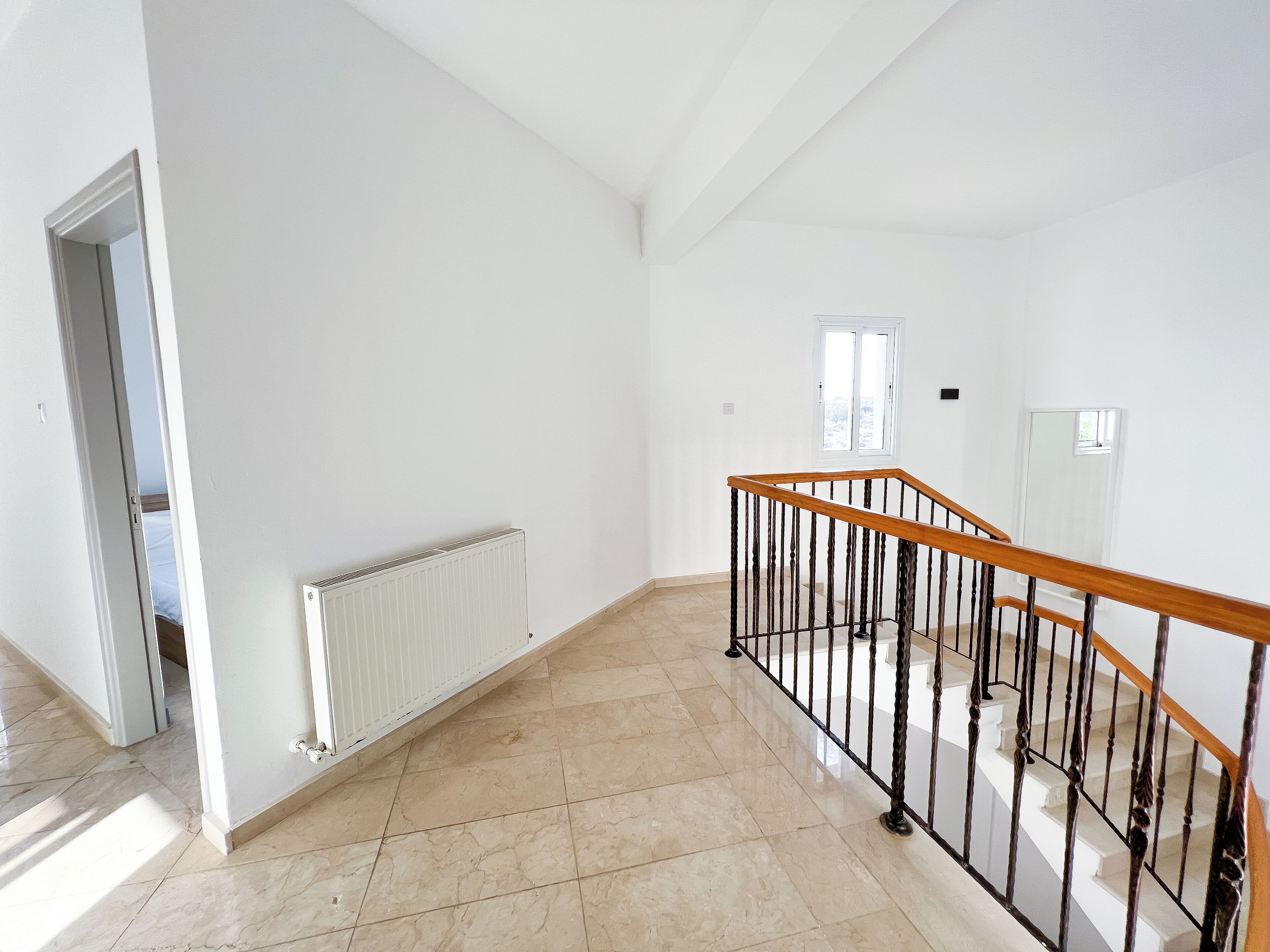 Una habitación amplia con piso de baldosas, una escalera de madera con barandal negro y un radiador blanco.