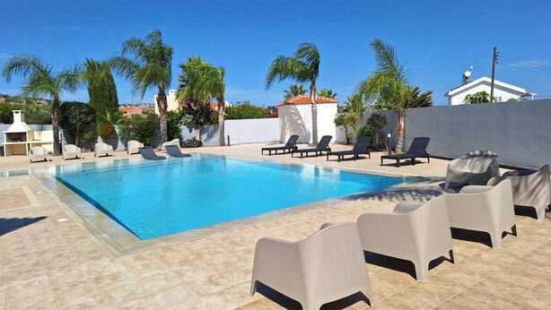 Una piscina con sillas de descanso, palmeras y un edificio blanco al fondo.