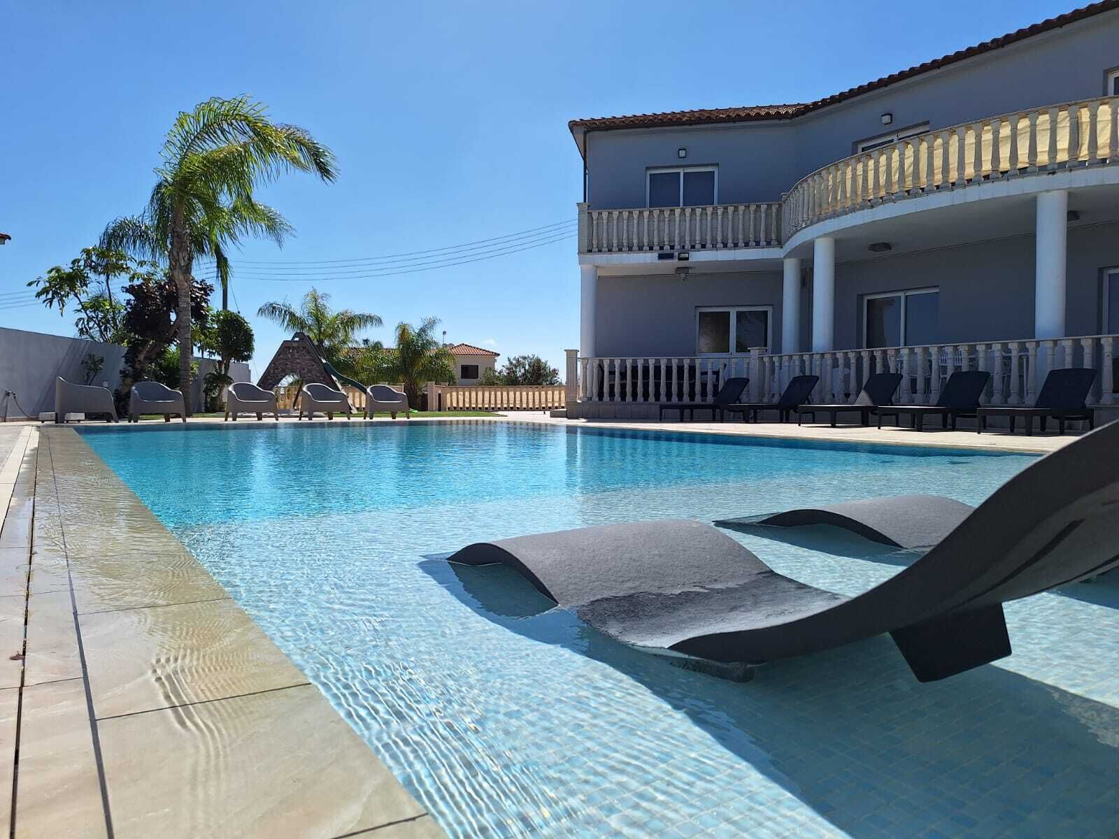 Une piscine avec des chaises longues, un palmier et un bâtiment doté d’un balcon.