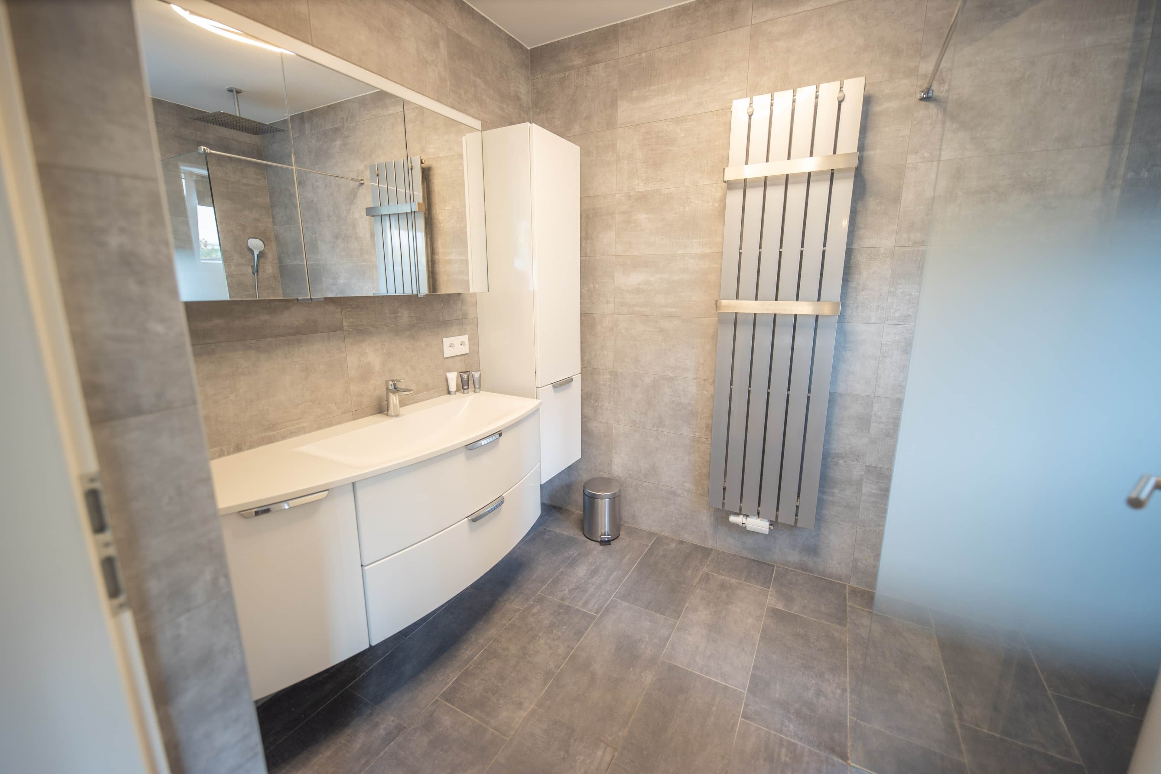 Un baño moderno con tocador curvo, un espejo grande, un perchero y una zona de ducha.