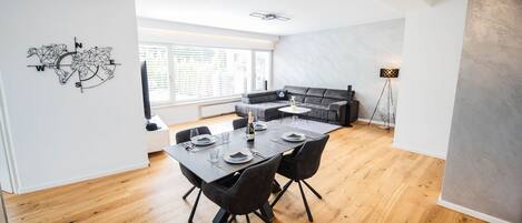 Un comedor moderno con piso de madera, una mesa redonda con sillas y un sofá negro al fondo.