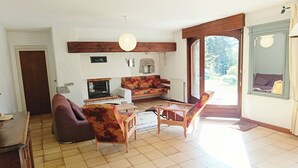 Een woonkamer met een open haard, een bank, stoelen, een houten tafel en een groot raam.