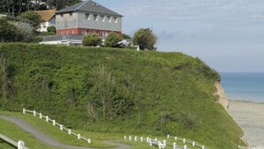 Un sendero costero con una cerca blanca, zonas verdes y un edificio al fondo.