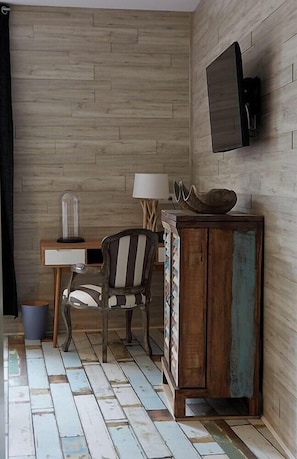 A room with a wooden floor, a desk with a lamp, a chair, a television mounted on the wall, and a cabinet. - Hotel The Originals Le Cise (Ault)