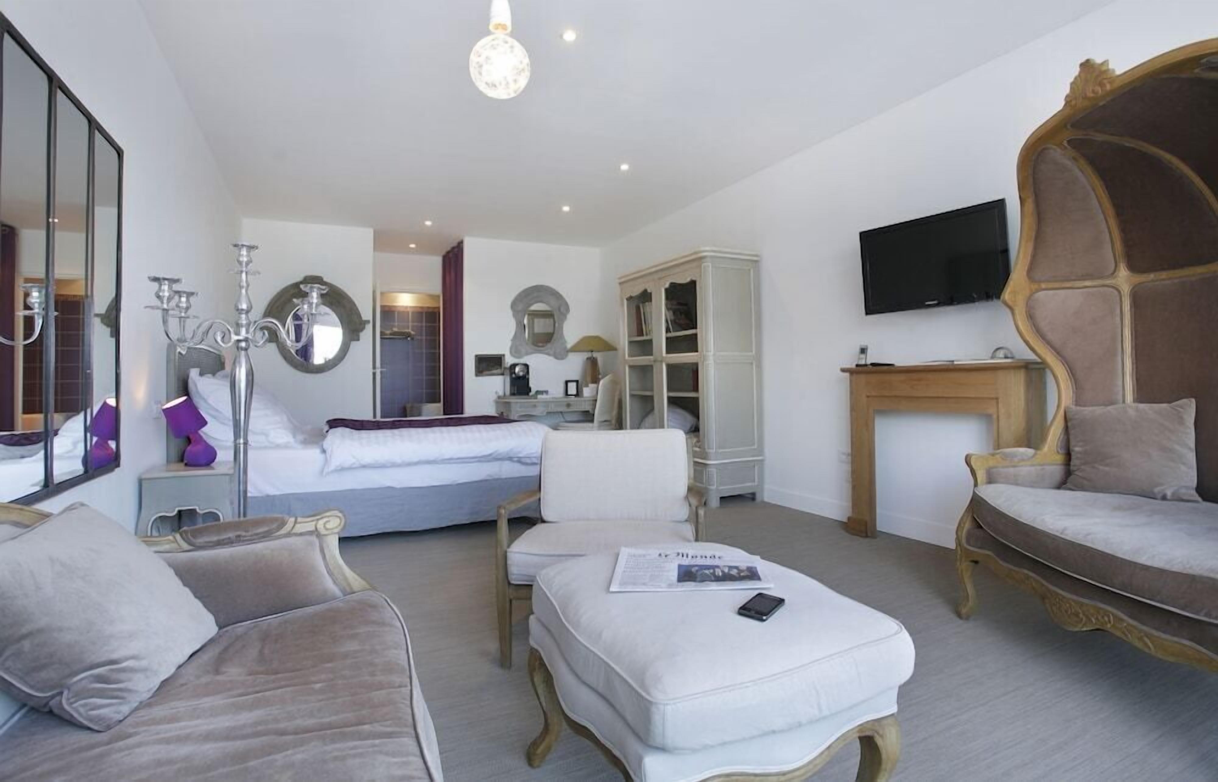 Une chambre d’hôtel avec un lit, deux canapés, une télévision, un miroir et un lustre.