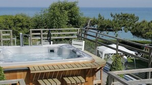 Una terraza de madera con hidromasaje, mobiliario exterior y vista al mar.