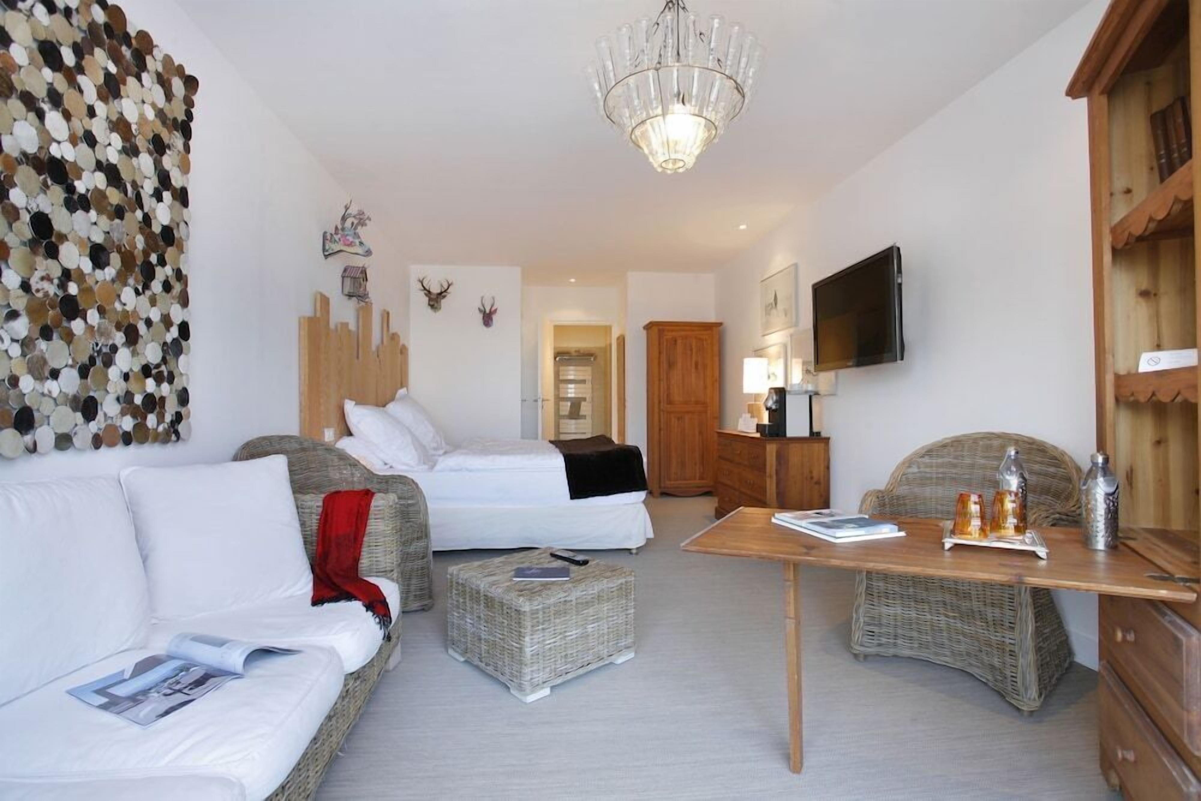 A hotel room with a bed, two sofas, a table, a TV, and a chandelier.
