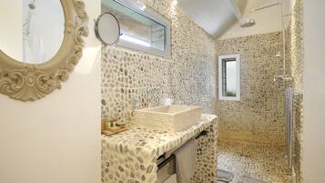 A bathroom with a stone-patterned wall, a large mirror, a sink, and a shower.
